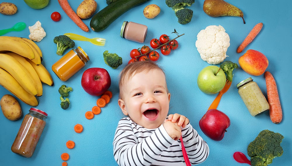 Bebé riendo rodeado de frutas y verduras