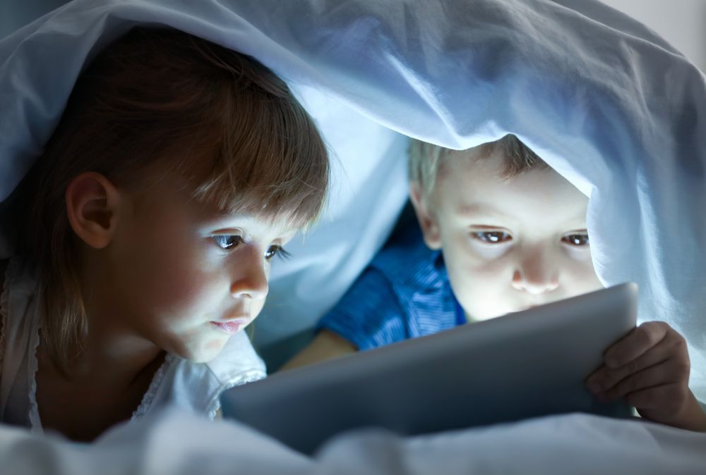 Niños debajo de las sábanas mirando una tablet