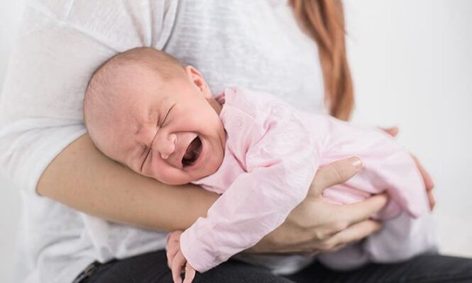Bebé llorando boca-abajo en los brazos de su madre