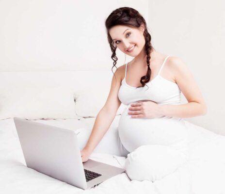 Mujer embarazada creando lista de nacimiento en portatil